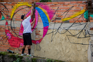 Artista realizando pintura grafite no muro da Java. Levante da Java, Galeria Providência, 2022. 